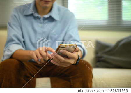 Smiling man using a smartphone while sitting in a relaxed living room 126851583