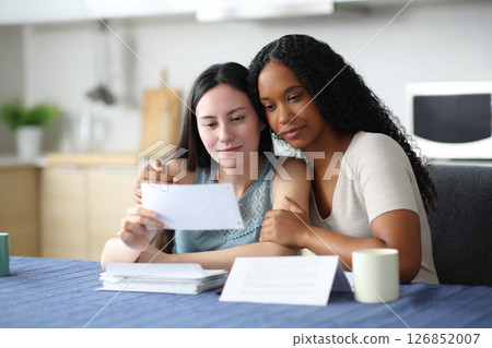 Interracial lesbian couple reading bank statement 126852007