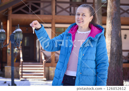 Woman Smiling with House Key in Front of Wooden Home Woman Smiling with House Key in Front of Wooden Home 126852612