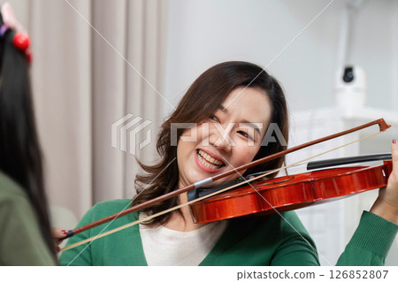 Joyful Music Education. Smiling mother plays violin while teaching daughter at home. Joyful Music Education. Smiling mother plays violin while teaching daughter at home. 126852807