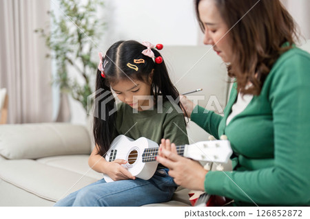 Music Education and Bonding. Mother teaching daughter to play ukulele at home. 126852872