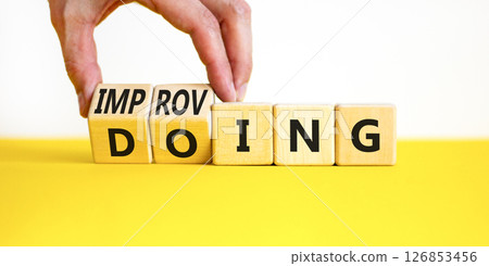 Doing or improving symbol. Businessman turns wooden cubes and changes the word Doing to Improving. Beautiful yellow table white background. Educational business doing or improving concept. Copy space 126853456