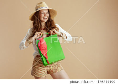 smiling trendy female in blouse and shorts against beige 126854499