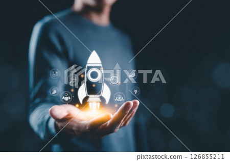 Startup Launch and Business Development Concept. Hand presenting glowing rocket icon with business symbols, representing startup launch, success, innovation, and strategic growth. business growth, 126855211
