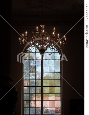 A stunning view of Chandelier hanging from the ceiling and Large arched stained glass windows in the background. A stunning view of Chandelier hanging from the ceiling and Large arched stained glass windows in the background. 126855232