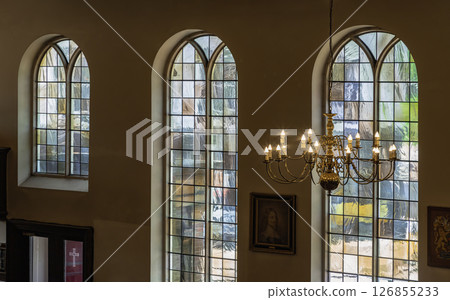 A stunning view of Chandelier hanging from the ceiling and Large stained glass windows in the background. 126855233