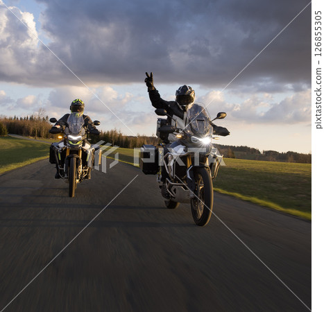 Driver riding motorcycle on empty road during sunset, spring mountains 126855305