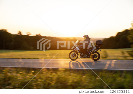 Driver riding motorcycle on empty road during sunset, spring mountains Driver riding motorcycle on empty road during sunset, spring mountains 126855311