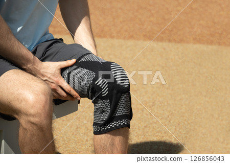 Man putting knee brace to support painful leg. Athlete bodybuilder leg wearing knee support brace or elastic kneecap bandage. Sleeve for compression. Health problems and pain. 126856043