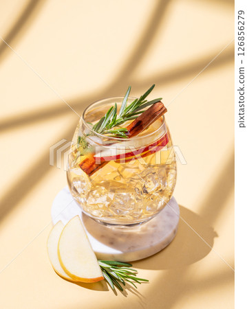 Apple cocktail or cider in a glass with ice, cinnamon and rosemary on a marble stand 126856279
