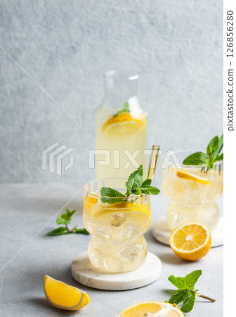Two glasses of fresh drink lemonade with lemon, mint and ice on a light background with bottle Two glasses of fresh drink lemonade with lemon, mint and ice on a light background with bottle 126856280