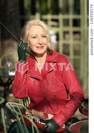 Gray-haired woman in her sixties in a red leather jacket in a restaurant in the city Gray-haired woman in her sixties in a red leather jacket in a restaurant in the city 126856574