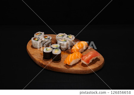 Creative minimalist display of assorted sushi rolls on a wooden platter against a dark backdrop, emphasizing vibrant colors and exquisite Japanese culinary art with a modern aesthetic. 126856658