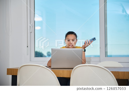 Confident Woman Working Remotely from Home Using Laptop and Smartphone Confident Woman Working Remotely from Home Using Laptop and Smartphone 126857033