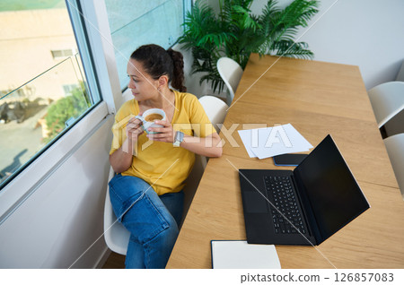 Woman Reflecting by Window During Coffee Break in Cozy Workspace 126857083
