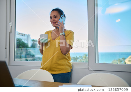 Confident Woman in Casual Office Setting Holding Coffee and Phone 126857099