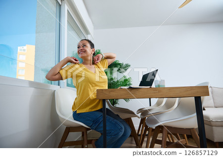 Smiling Woman Stretching in Home Office with Laptop During Work Break 126857129