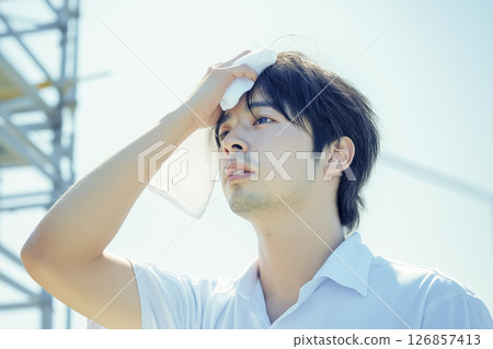 A worker wipes off sweat while working outdoors in midsummer 126857413
