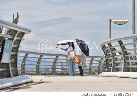 Two women with parasols looking out at the sea from the Nishihama pedestrian bridge in Shonan 126857534