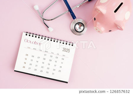October 2025 desk calendar and stethoscope with piggy bank, Savings for health. 126857632
