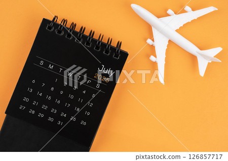 July 2025 black desk calendar and airplane toy on orange background. Travel concepts. July 2025 black desk calendar and airplane toy on orange background. Travel concepts. 126857717