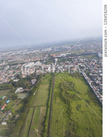 Aerial view of a suburban residential area surrounded by green fields and urban development under a cloudy sky. 126858206