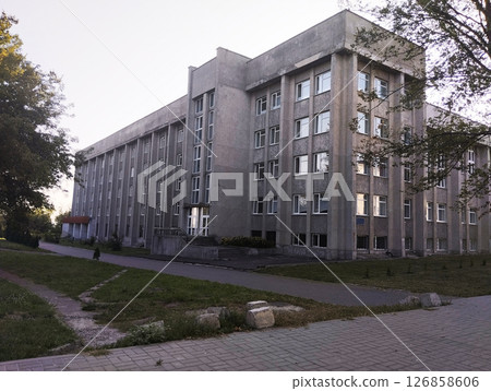 Large gray building on a background of blue sky and green trees Large gray building on a background of blue sky and green trees 126858606