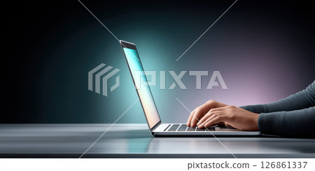 Person typing on modern laptop with glowing screen, sitting at desk in dark room, focused and productive atmosphere 126861337