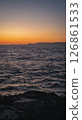 Rocky coastline meeting calm ocean under a vibrant sunset sky 126861533