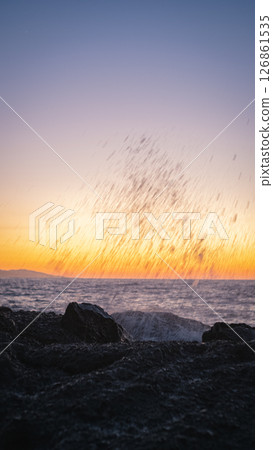 Waves crashing on rocks at sunset creating stunning water droplets Waves crashing on rocks at sunset creating stunning water droplets 126861535