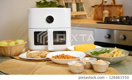 Modern air fryer cooking various dishes in kitchen: chicken, vegetables, and more 126861550