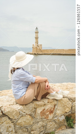 Tourist admiring chania lighthouse from venetian harbor wall in crete Tourist admiring chania lighthouse from venetian harbor wall in crete 126861557