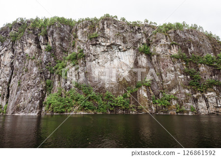 Steep fjord cliff face with green forest reflection near Bergen, Norway Steep fjord cliff face with green forest reflection near Bergen, Norway 126861592