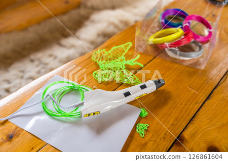 3D printing pen and colorful filaments on wooden table with green butterfly shape, selective focus 126861604
