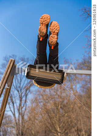 Child swinging upside down on swing seat in park, view from below, sunny winter day 126861618