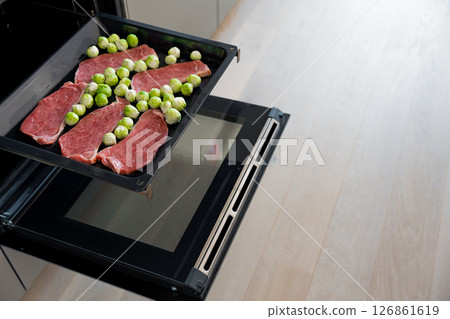 Raw pork steaks and Brussels sprouts on oven tray ready for roasting in kitchen, selective focus 126861619