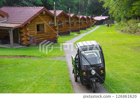 Small electric moped parked on pathway in front of rustic log cabins in the forest, selective focus 126861620