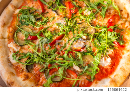 Close up of fresh vegetable pizza with arugula in cardboard box on wooden table, top view, sunlight Close up of fresh vegetable pizza with arugula in cardboard box on wooden table, top view, sunlight 126861622