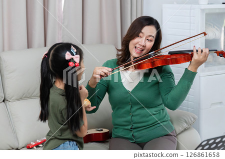 Musical Interaction. Mother and daughter enjoy playing violin together at home. 126861658