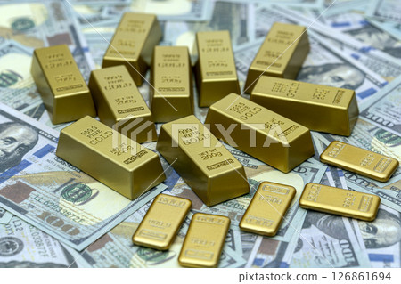 Gold bars are neatly arranged on background of dollar bills, symbolizing wealth and financial security. shiny gold bars contrast with paper currency, highlighting their value 126861694