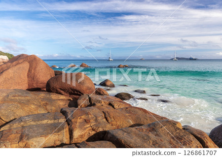 Coastal view featuring rocky shoreline, blue waters, and distant boats 126861707