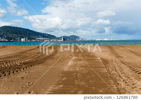 A wooden pathway and tire tracks lead towards the sea on a tranquil, cloudy beach. Getxo, Bilbao 126861780