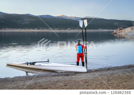 male rower and a coastal rowing shell on a rocky shore of Carter Lake in fall or winter scenery in northern Colorado. 126862388