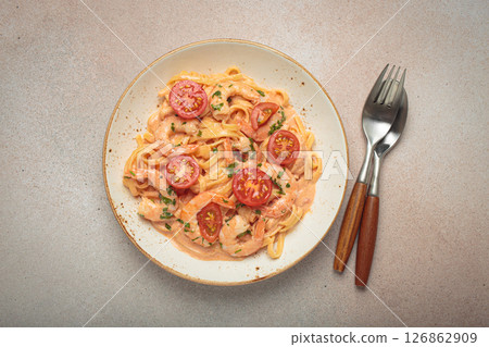 Seafood pasta linguine with shrimps and cherry tomatoes in creamy sauce garnished with parsley on white plate on light warm beige background top view 126862909