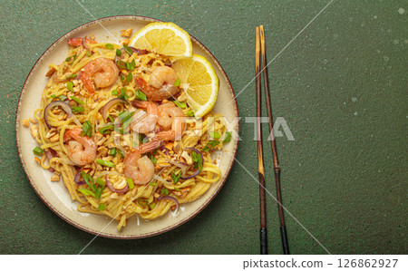 Pad thai noodles with shrimps and chopsticks on rustic green background, traditional dish of Thailand, space for text Pad thai noodles with shrimps and chopsticks on rustic green background, traditional dish of Thailand, space for text 126862927