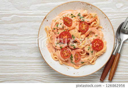 Seafood pasta linguine with shrimps and cherry tomatoes in creamy sauce garnished with parsley on white plate on white wooden background top view, space for text 126862956