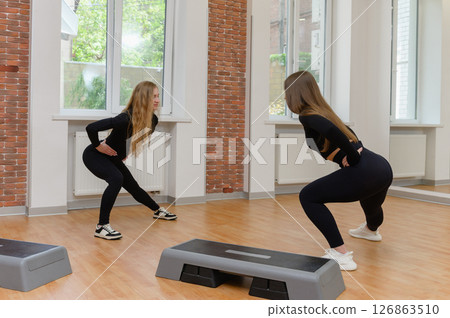 Two women doing side lunges during fitness workout. Two women doing side lunges during fitness workout. 126863510