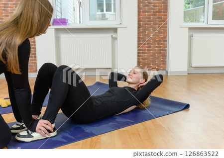 Woman doing sit-ups with partner support in gym studio. Woman doing sit-ups with partner support in gym studio. 126863522