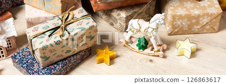 Rustic-themed Christmas gift boxes in natural tones resting beneath a Christmas tree, surrounded by a calm, minimalist holiday atmosphere, banner 126863617