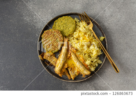 A wholesome breakfast featuring turmeric rice with baked ocean fish, complemented by broccoli pancakes and roasted vegetables, offering a nutritious and satisfying meal 126863673
